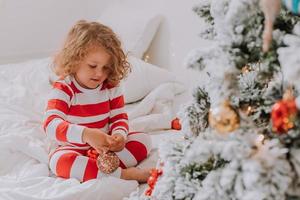 poco ragazza nel Natale a strisce pigiama decora il Natale albero. stile di vita. alto qualità foto