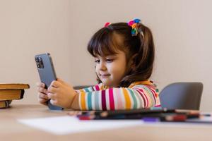 un' carino poco ragazza è impegnato con un' insegnante in linea di Telefono. in linea formazione scolastica di bambini. bambini in età prescolare e gadget. alto qualità foto