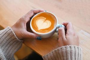 latte macchiato arte donna caffè con mano Tenere un' tazza su il legna tavolo, latte macchiato caffè con cuore nel caffè tazza per amore caffè concetto nel il mattina foto