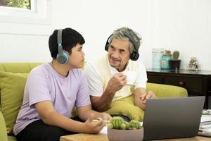 asiatico anziano Nonno e il suo figlio siamo la spesa volte insieme a casa per Collegare cuffie con il suo il computer portatile per orologio e per giocare in linea Giochi, morbido e selettivo messa a fuoco, raccolta adolescenti concetto. foto