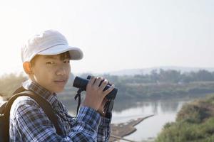 asiatico ragazzo è utilizzando binocolo per fare il uccelli' Guardando nel tropicale foresta durante estate campo, idea per apprendimento creature e natura animali e insetti al di fuori il aula. foto