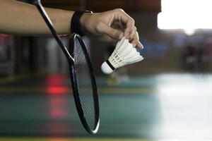 badminton giocatore detiene bianca crema volano e racchetta nel davanti di il netto prima servendo esso per un altro lato di il Tribunale, morbido e selettivo messa a fuoco su volano. foto