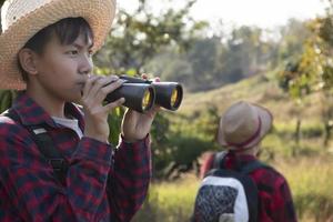 asiatico ragazzi siamo utilizzando binocolo per fare il uccelli' Guardando nel tropicale foresta durante estate campo, idea per apprendimento creature e natura animali e insetti al di fuori il aula. foto