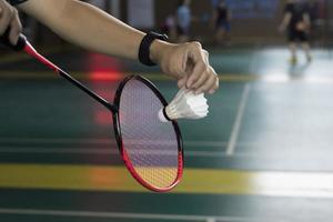 badminton giocatore detiene bianca crema volano e racchetta nel davanti di il netto prima servendo esso per un altro lato di il Tribunale, morbido e selettivo messa a fuoco su volano. foto