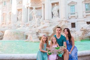 famiglia con turistico carta geografica vicino fontana di trevi, Roma, Italia. contento padre e bambini godere italiano vacanza vacanza nel Europa. foto