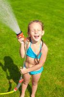 contento carino poco ragazza scrosciante acqua a partire dal un' tubo flessibile e ridendo foto