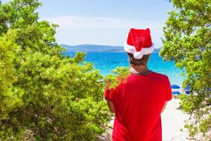 giovane uomo nel rosso Natale cappello su tropicale spiaggia vicino il abeti foto