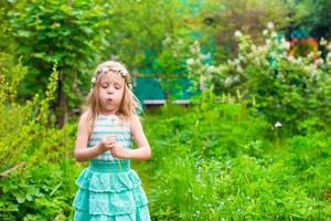 adorabile poco ragazza soffiaggio un' dente di leone nel il giardino foto