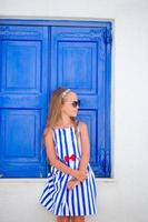 adorabile poco ragazza nel davanti di blu porta all'aperto a tipico greco tradizionale villaggio su mykonos nel Grecia foto