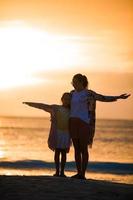 poco ragazza e contento madre silhouette nel il tramonto a il spiaggia foto