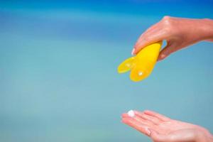 mani femminili con la bottiglia di crema solare sfondo blu mare foto