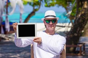 giovane uomo su il spiaggia con tavoletta computer. mostrando schermo digitale pc foto