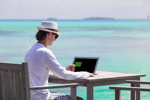 giovane uomo Lavorando su il computer portatile con credito carta durante tropicale vacanza foto