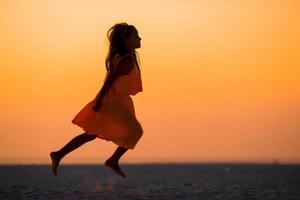 silhouette di adorabile poco ragazza su bianca spiaggia a tramonto foto