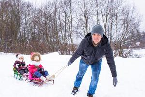 giovane padre con poco figlie slittino nel inverno all'aperto foto