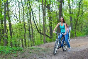 madre e poco figlia Ciclismo bicicletta a il parco foto