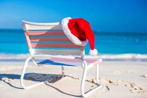avvicinamento rosso Santa cappello su sedia longue a tropicale spiaggia foto