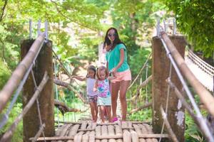 giovane madre con sua poco ragazze su sospensione ponte al di sopra di il fiume lobo, Filippine foto