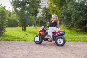 bellissimo poco ragazza avendo divertimento su sua giocattolo bicicletta nel verde parco foto