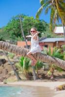 adorabile poco ragazza seduta su palma albero durante estate vacanza su bianca spiaggia foto