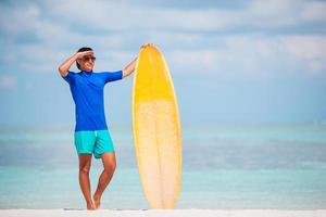 giovane Surf uomo a bianca spiaggia con giallo tavola da surf foto