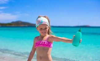 poco adorabile ragazza nel costume da bagno con abbronzatura lozione bottiglia foto