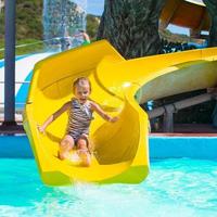 poco ragazza su acqua diapositiva a Parco acquatico durante estate vacanza foto