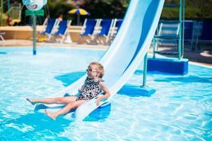 poco ragazza su acqua diapositiva a Parco acquatico su estate vacanza foto