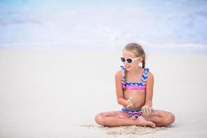 adorabile poco ragazza giocando con sabbia su il spiaggia. ragazzo seduta nel superficiale acqua e fabbricazione un' castello di sabbia foto