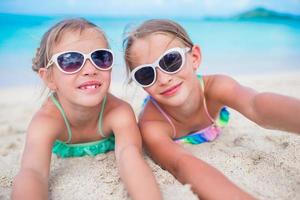 adorabile poco sorelle a spiaggia durante estate vacanza dire bugie su caldo sabbia foto