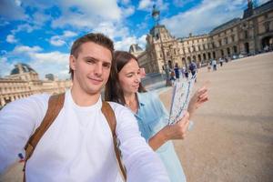contento giovane famiglia con carta geografica di europeo città assunzione autoscatto nel Parigi foto