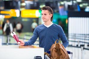 giovane uomo con passaporti e imbarco passa a il davanti scrivania a aeroporto foto