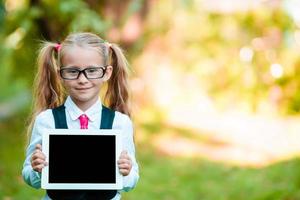 adorabile poco ragazza Tenere tavoletta pc all'aperto nel autunno soleggiato giorno foto