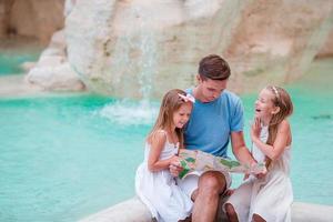 famiglia con turistico carta geografica vicino fontana di trevi, Roma, Italia. contento padre e bambini godere italiano vacanza vacanza nel Europa. foto