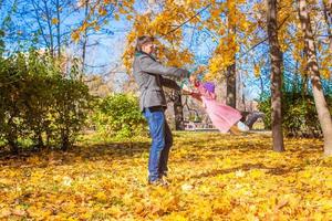 poco ragazza con contento padre avendo divertimento nel autunno parco su un' soleggiato giorno foto