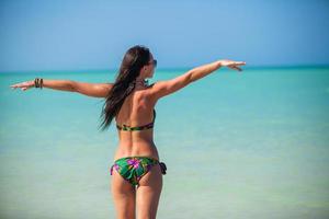 giovane donna godendo il vacanza diffusione sua mani su un' bianca, tropicale spiaggia foto