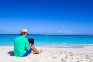 giovane che lavora al computer portatile in spiaggia tropicale foto