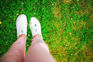 avvicinamento di femmina gambe nel scarpe da ginnastica su il erba all'aperto nel il parco. foto