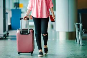 avvicinamento aereo passeggeri con passaporti e imbarco passaggio e rosa Bagaglio nel un aeroporto sala. giovane donna nel internazionale aeroporto a piedi con sua bagaglio. foto