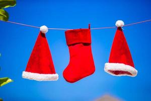 rosso Santa cappelli e Natale calza sospeso su tropicale spiaggia fra palma alberi foto