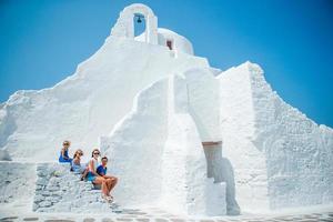 famiglia vacanza nel Europa. genitori e bambini a strada di tipico greco tradizionale villaggio con bianca muri e colorato porte su mykonos isola foto