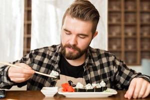 uomo mangiare Sushi rotoli utilizzando bambù bastoni nel un' ristorante. giapponese cucina foto