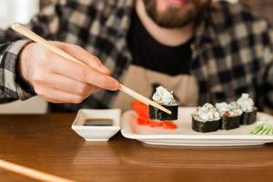 vicino su di Sushi rotoli su un' tavolo nel un' ristorante. uomo mangiare Sushi rotoli utilizzando bambù bastoni. giapponese cucina foto