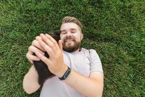 uomo con poco gattino dire bugie e giocando su erba - amicizia amore animali e animale domestico proprietario concetto foto