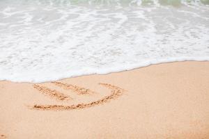 contento Sorridi disegno su il sabbia a tropicale spiaggia foto