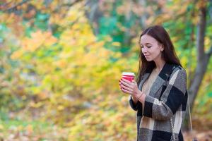 autunno concetto - bellissimo donna potabile caffè nel autunno parco sotto autunno fogliame foto