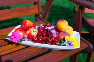 piatto con fresco frutta e fiori su di legno sedie nel il giardino foto