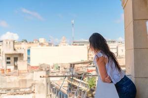 giovane attraente donna su vecchio balcone nel appartamento nel havana con gareggiare di vecchio cittadina e case foto