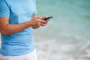 giovane uomo utilizzando mobile Telefono mentre a piedi su il spiaggia. avvicinamento smartphone nel mani foto