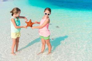 adorabile poco ragazze avendo divertimento su il spiaggia pieno di stella marina su il sabbia foto